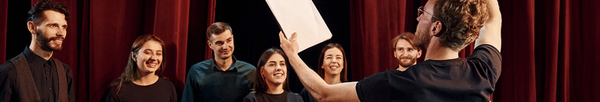 Man with notepad practice his role. Group of actors in dark colored clothes on rehearsal in the theater.